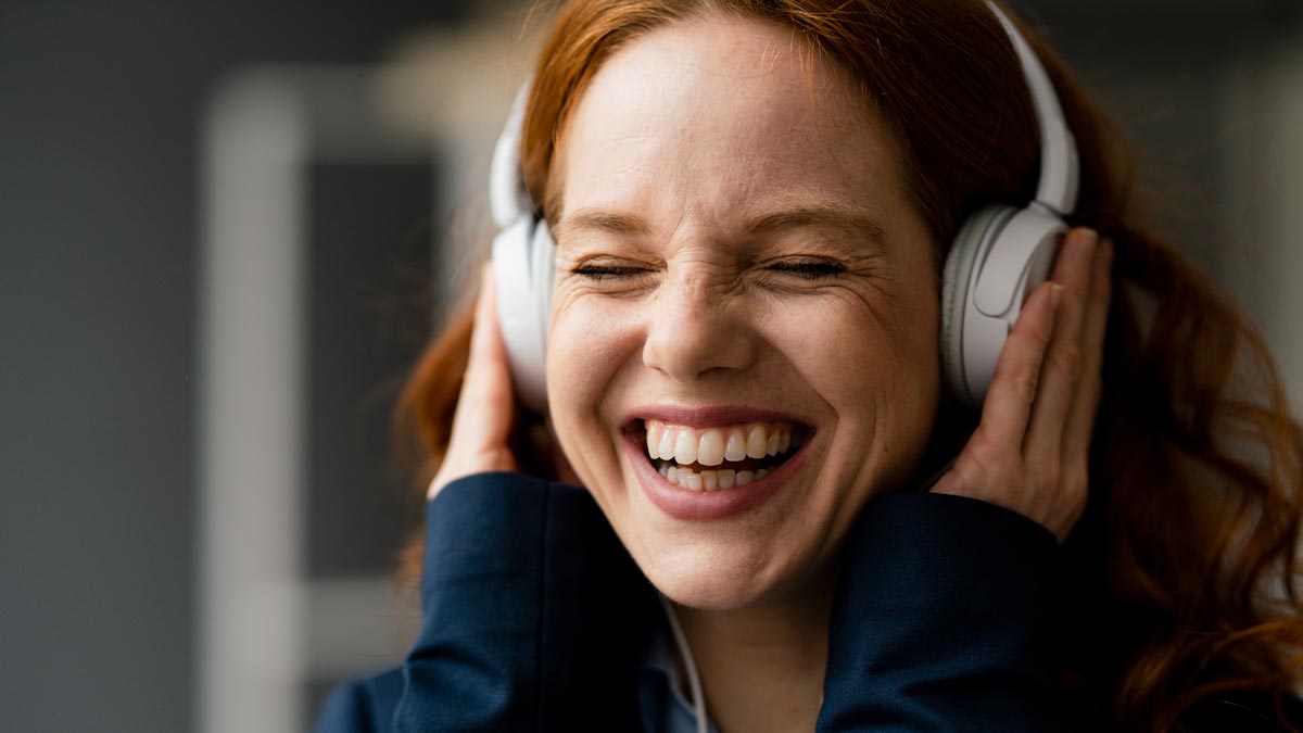 emotional reaction to music concept a white woman with red hair listening to music on headphones with a big smile on her face