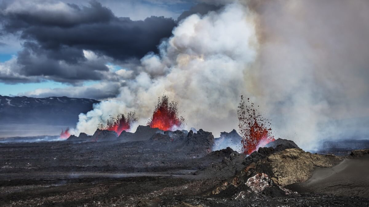 volcano fissure erupting venting gases, smoke and aerosols into the atmosphere with clouds in the background