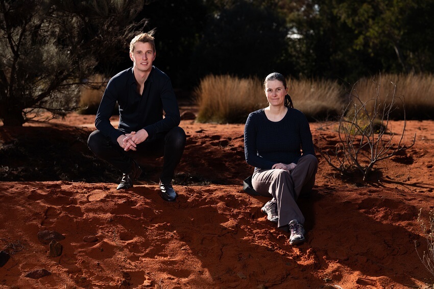 Two people sitting in a garden with lots of red dirt