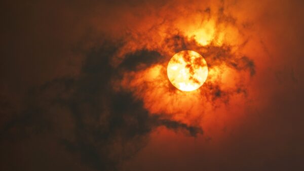 Sun through dark smoke clouds from bush fire with red glow, climate change in Australia