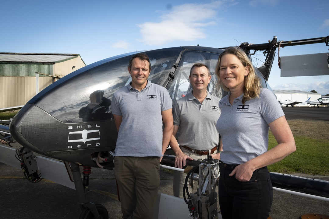 Three people in grey t-shirts stand in front of electric flying vehicle amsl aero