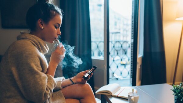 young woman vaping while looking at smartphone