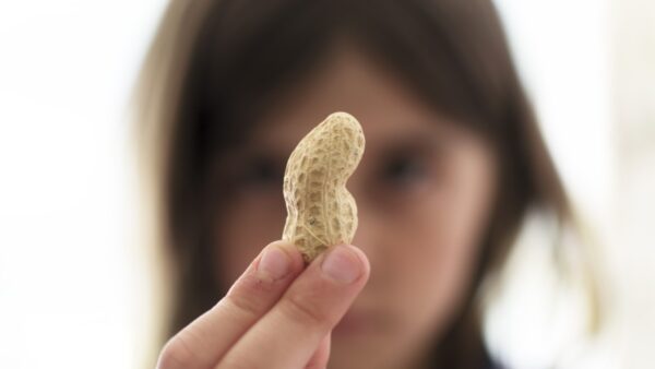 Out of focus photograph of a young girl with brown hair. She is holding a peanut in focus in front of her face.