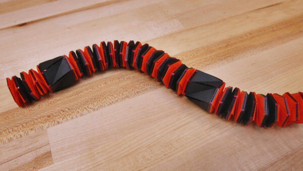 a segmented black and red caterpillar like robot on wood floor