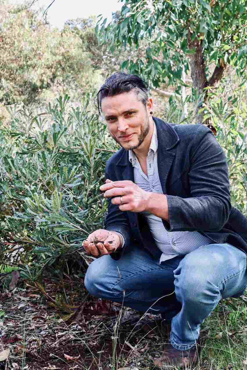 person crouches outside with handful of soil