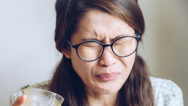 Photograph of a woman wearing glasses, pulling a face after drinking bitter coffee.
