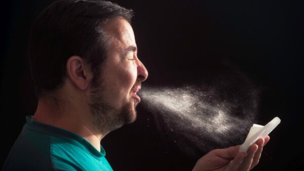 Man sneezing on dark background backlit with visible sneeze particles