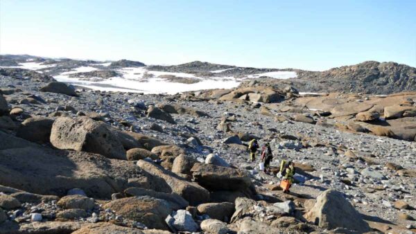 Photograph of people hiking across a rocky peninsula, where snow can be seen in the distance