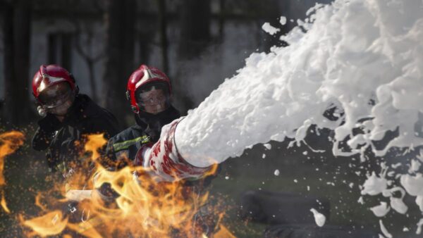 Photograph of two firefighters spraying fire-suppressing foam on a fire